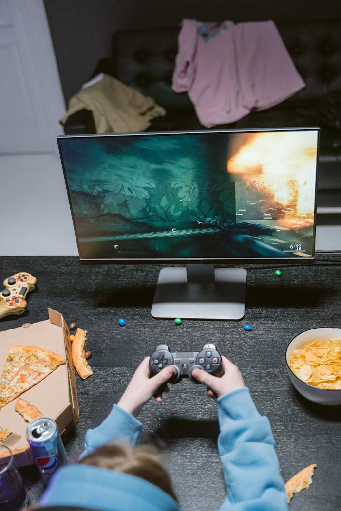 Person gaming indoors with snacks and game controller, showcasing modern technology and leisure.